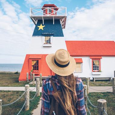 A person looking out at a lighthouse painted in the colours of the Acadien flag.
